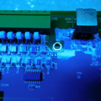 De vernisrobot vliegt over de print, maar er is wel een speling nodig (moet vernist/mag niet vernist) van een 5-tal mm, hier moet het gemetalliseerde bevestigingsgat vrij blijven van vernis. Bemerk ook: op hoge componenten (links boven) kan een vernisrobot moeilijk volledig dekkend vernissen.